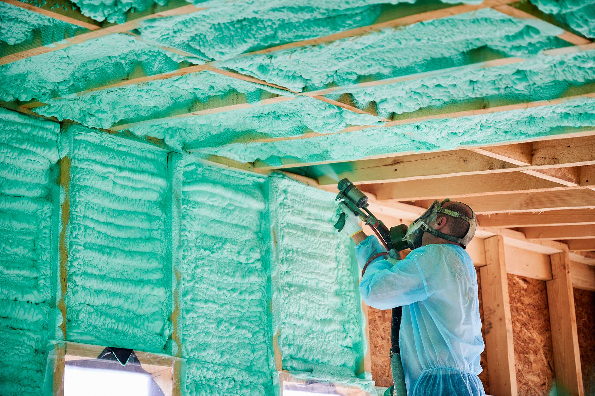 Male builder insulating wooden frame house. Man worker spraying polyurethane foam inside of future cottage, using plural component gun. Construction and insulation concept.